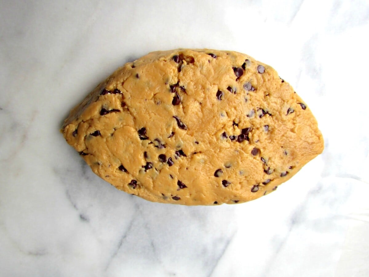 A mound of chocolate chip cookie dough shaped like a football sits on a white marble surface, perfect as a football dip for game day celebrations.