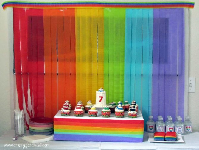 rainbow birthday party cake table with rainbow background