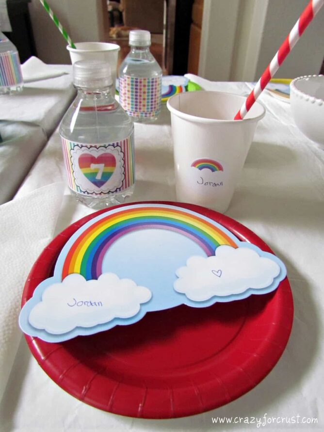 rainbow birthday party place setting with red plate, decorated water bottle and place card