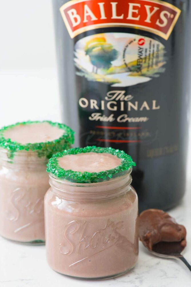 baileys pudding shots in shot glasses with a bottle of Baileys' Irish cream in the background