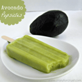 Avocado popsicle missing one bite on a white plate, with an avocado in the background, graphic title on the top right.
