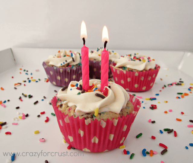 Funfetti cake batter pie with two pink candles lit and more cupcake pies in background