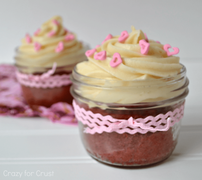 pink velvet cupcakes in jars with cream cheese frosting and pink heart sprinkles, wrapped with a pink bow with words on photo
