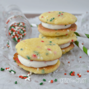 Funfetti sandwich cookies on a white napkin with holiday sprinkles poured around them.