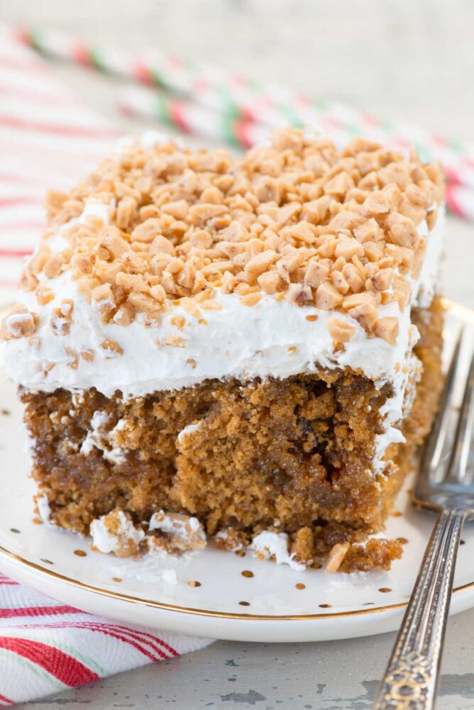 A Gingerbread Poke Cake slice on white plate with gold dots and fork and christmas napkin