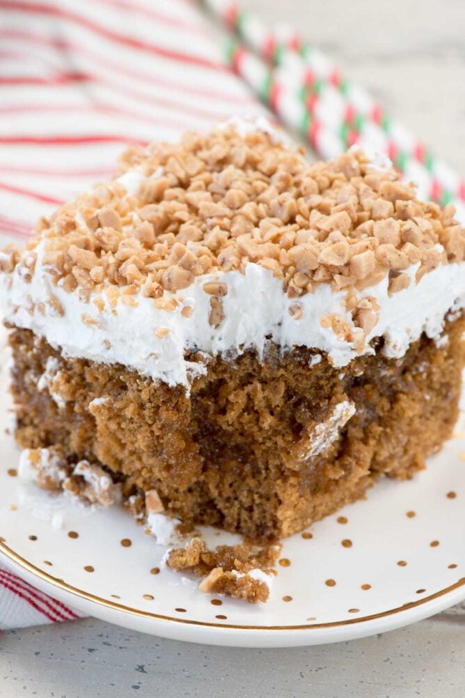 A Gingerbread Poke Cake slice on white plate with gold dots and fork and christmas napkin