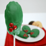 Madeline cookies coated with green frosting and red hots to look like holiday wreaths on a white plate, with graphic title on the top right.