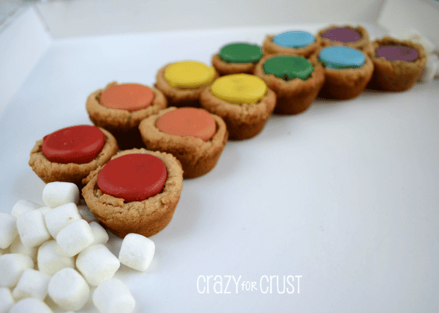 peanut butter cookies cups with rainbow colored candies in the center in the shape of a rainbow with marshmallow clouds