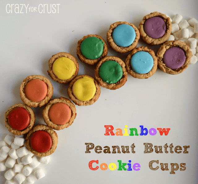 peanut butter cookies cups with rainbow colored candies in the center in the shape of a rainbow with marshmallow clouds