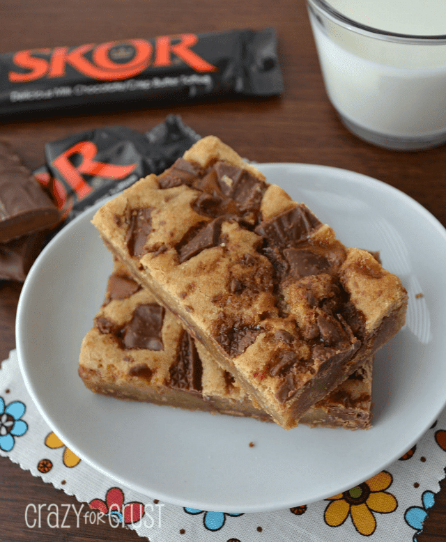 A plate of blondies next to candy bars and a glass of milk.