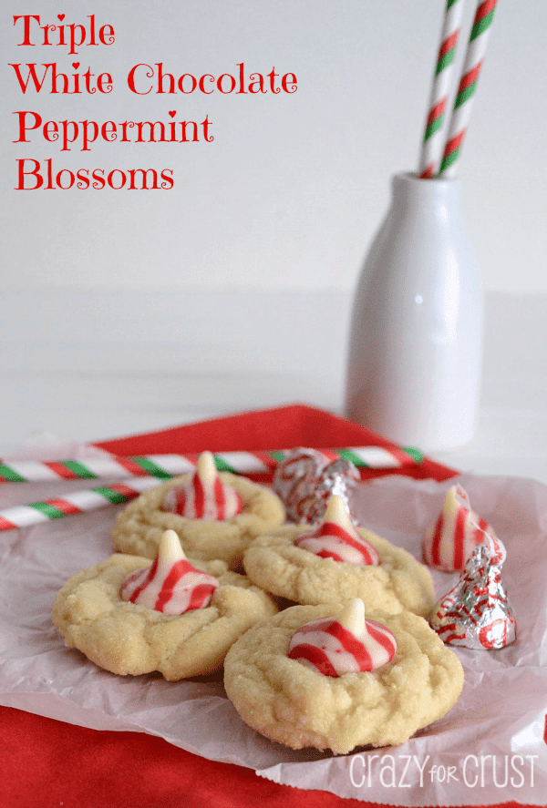 Triple White Chocolate Peppermint Blossoms on white parchment paper with ingredients and festive straws around cookies