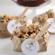 Peanut butter kitchen sink popcorn in a brown paper bag with a clothespin holding a football graphic, graphic title on the bottom.