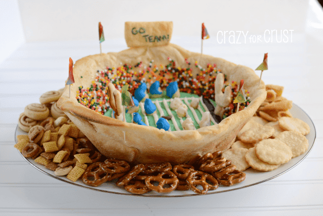 Snackadium made out of crescent rolls with icing field and sprinkle people on white plate with pie crust and cracker dippers