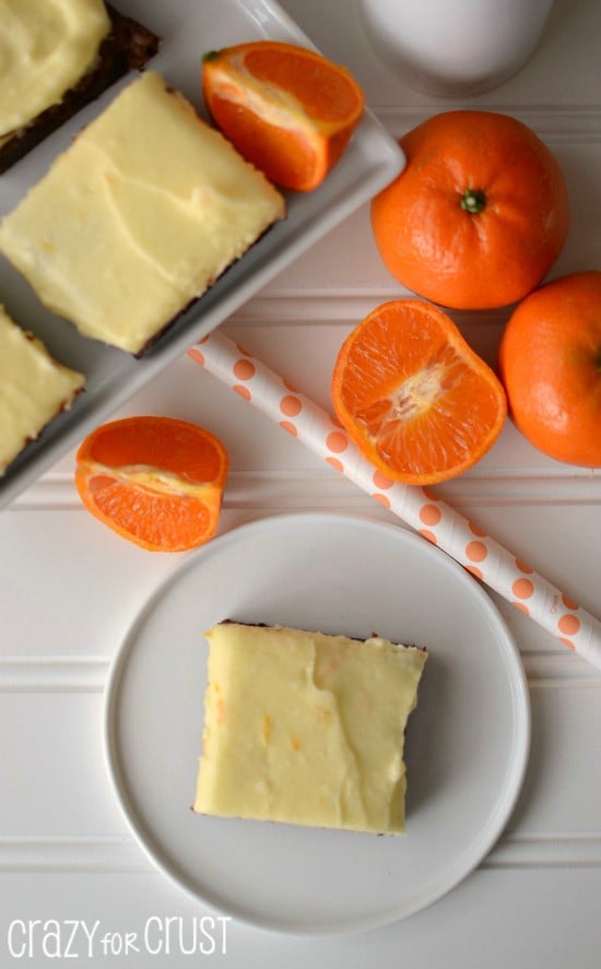 orange frosted brownies on white plate with oranges in background