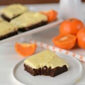 orange frosted brownies on white plate with oranges in background