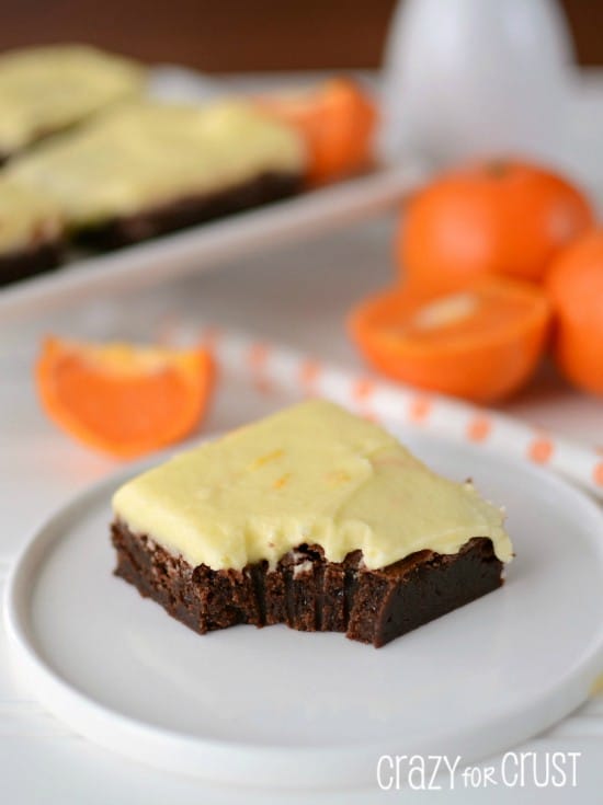 orange frosted brownies on white plate with oranges in background