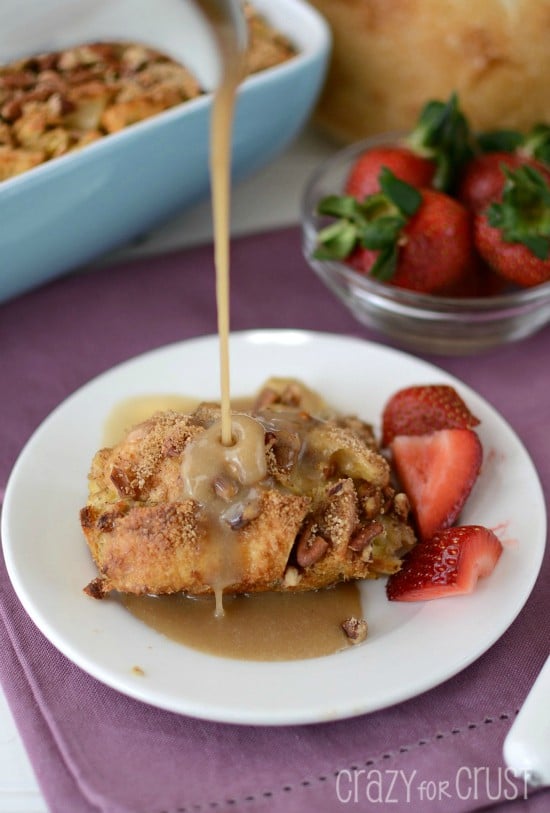 banana baked french toast on white plate with berries with syrup pouring on