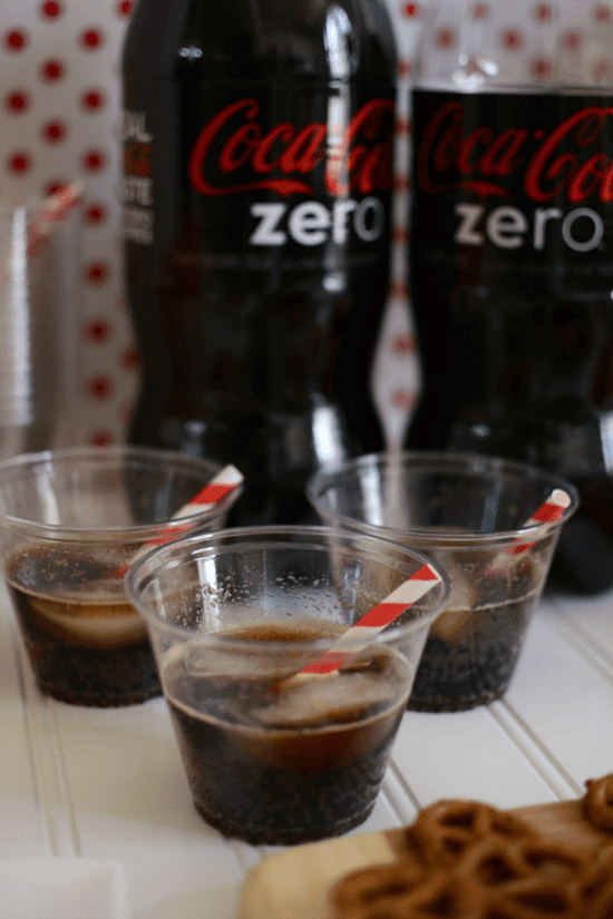Three clear plastic cocktail cups of coke zero with red and white straws on party table