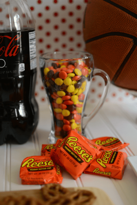 Reese's pieces in a glass soda cup with Reese's cups in a pile in front of it