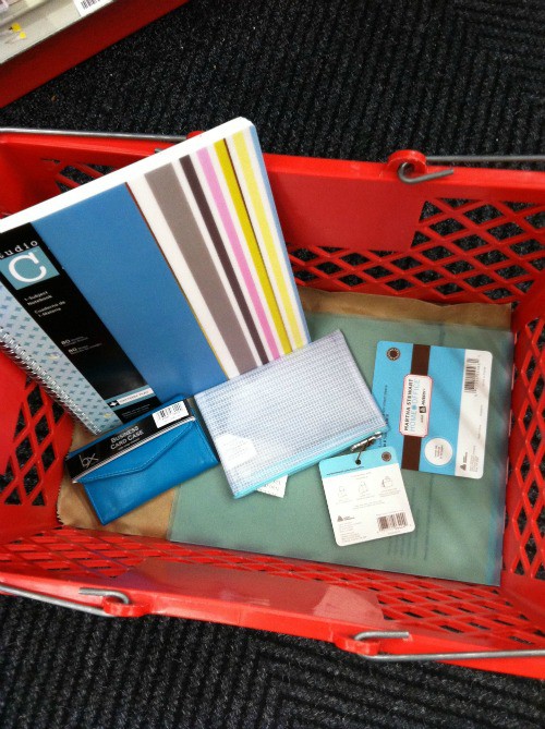 Red shopping basket filled with office supplies like notebooks and pencil case