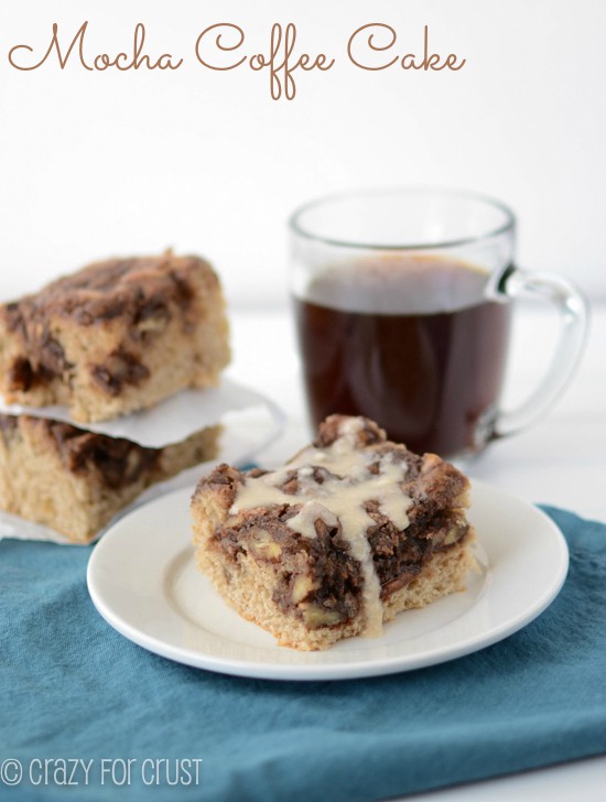 Mocha Coffee Cake slice on a white plate with more pieces behind and a cup of coffee in the background