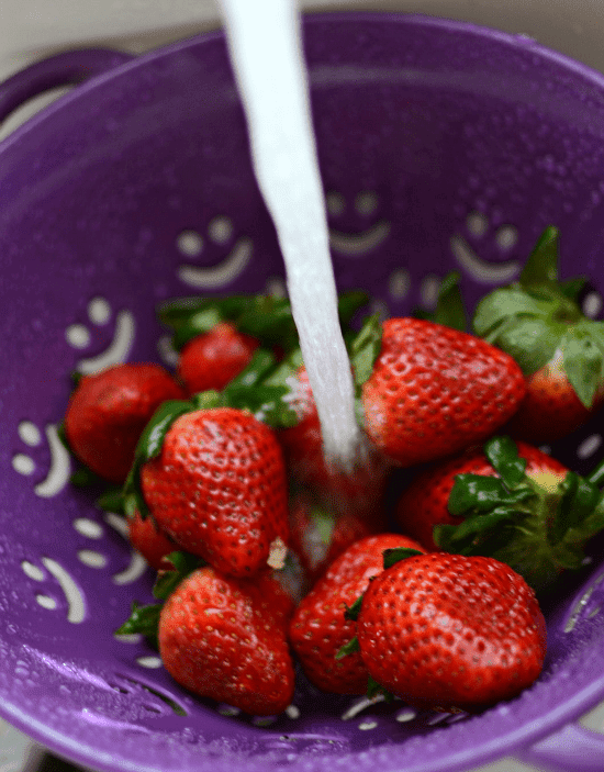 Fresh strawberries being washed in a purple smiley face colander 