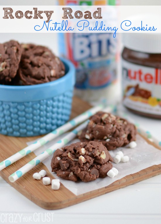 Rocky Road Nutella Pudding Cookies on wood cutting board with ingredients in the background and recipe title on top of photo