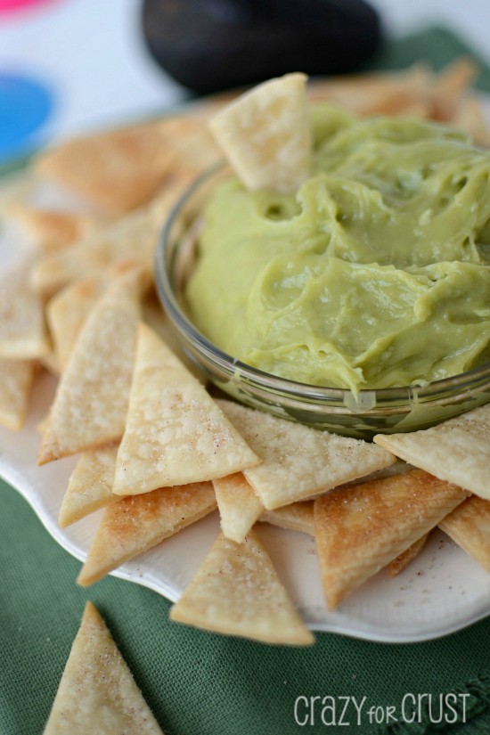 Closeup photo of Sweet Guacamole Dip in a glass bowl with Pie Crust Tortilla Chips around it on a white serving plate 