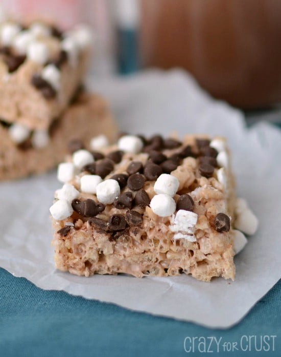 Hot Chocolate Krispie Treats with marshmallows and chocolate chips on parchment paper with hot cocoa in back