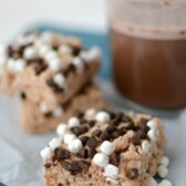 Hot Chocolate Krispie Treats with marshmallows and chocolate chips on parchment paper with hot cocoa in back