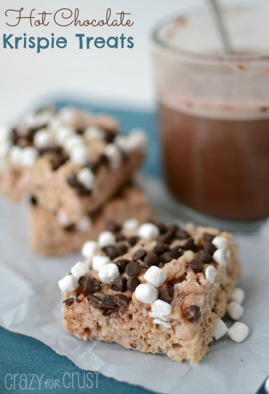 Hot Chocolate Krispie Treats with marshmallows and chocolate chips on parchment paper with hot cocoa in back