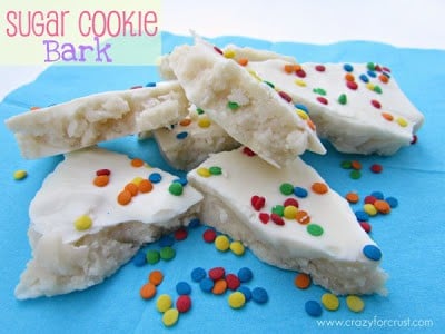 Sugar Cookie Bark on blue napkin with rainbow sprinkles and recipe name in top left corner