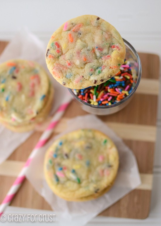 Overhead shot of Thin Sugar Cookies, two on cutting board and one on cup of sprinkles