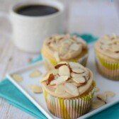 almond cupcakes with caramel frosting and almonds on top on white plate with teal napkin and coffee behind