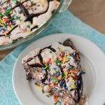 slice of ice cream pie on white plate with hot fudge and sprinkles