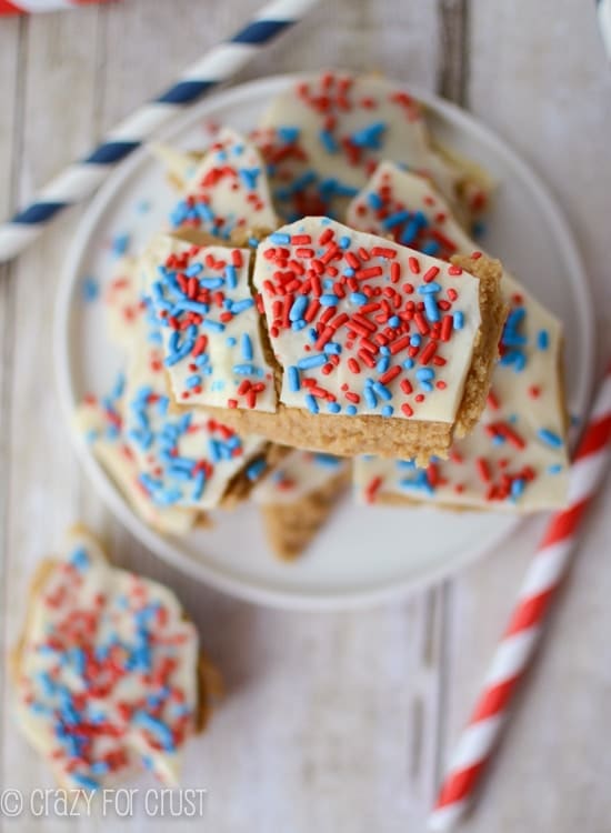 Overhead shot of Patriotic Peanut Butter Cookie Dough Bark on a white plate with red and blue striped straws on table