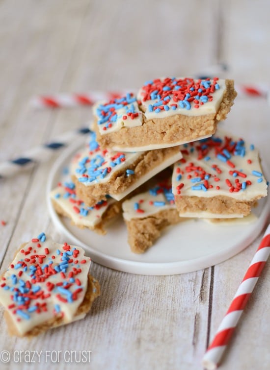 Stack of Patriotic Peanut Butter Cookie Dough Bark on white plate on whitewashed wooden table with straws
