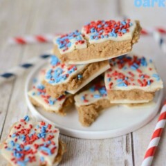 Stack of patriotic peanut butter cookie dough bars with red and blue sprinkles on a white plate on white wood table with words on top of photo