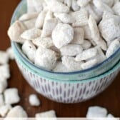 cinnamon roll muddy buddies coated in powdered sugar in two bowls on brown table