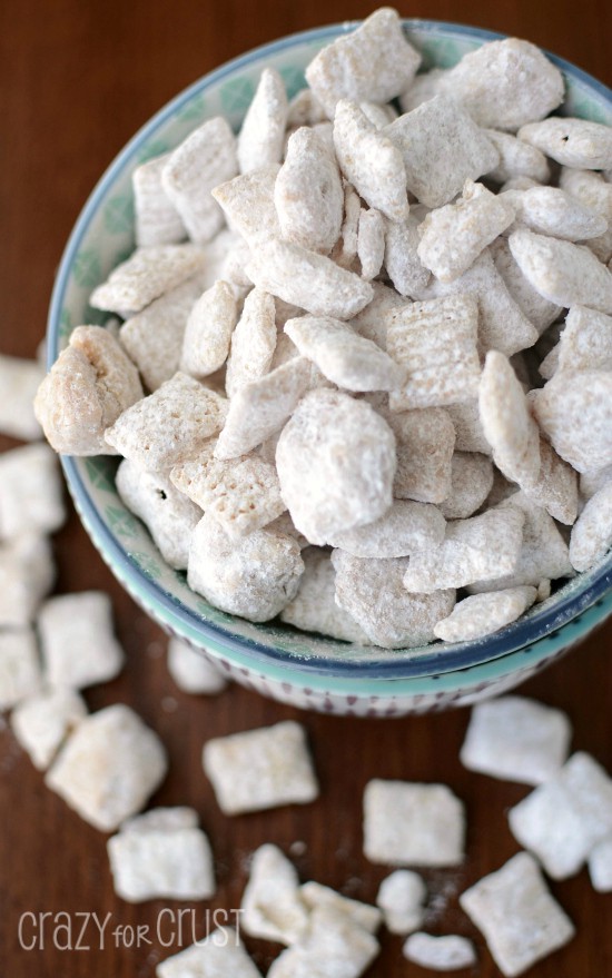 cinnamon roll muddy buddies coated in powdered sugar in two bowls on brown table