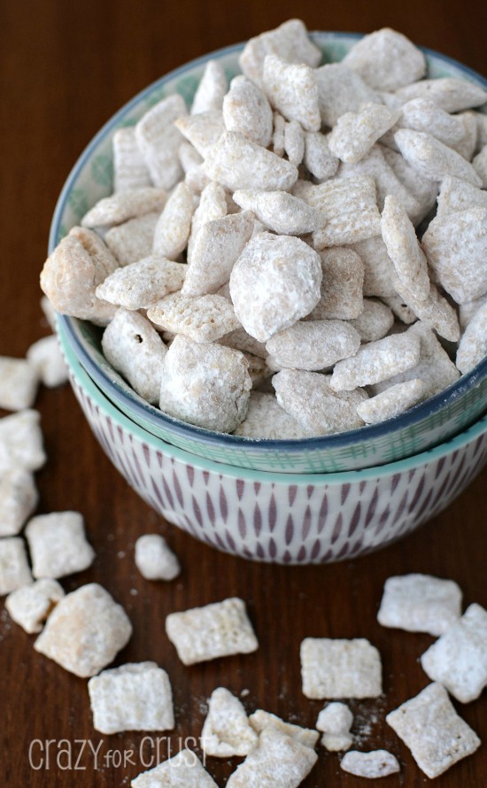 cinnamon roll muddy buddies coated in powdered sugar in two bowls on brown table