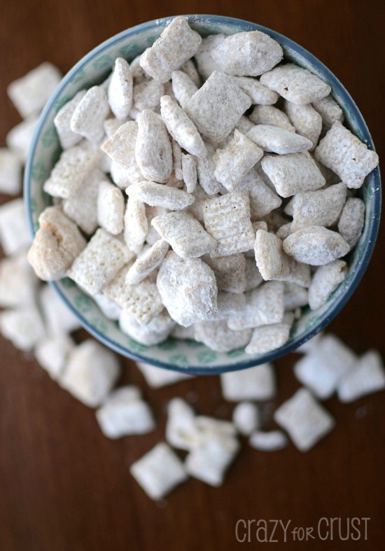 Overhead shot of cinnamon roll muddy buddies coated in powdered sugar in two bowls on brown table