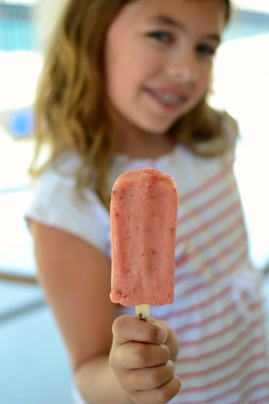 Girl holding a pink popsicle with the focus on the popsicle