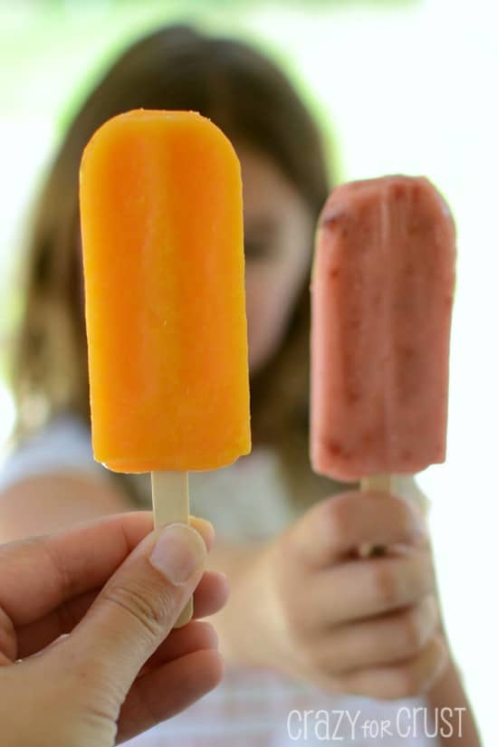 Two popsicles being held with girl in the background out of focus