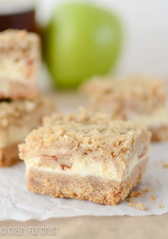 stack of bars with crust, apple cheesecake and crumble topping on parchment