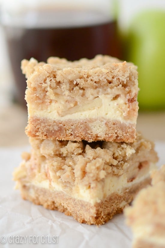 stack of bars with crust, apple cheesecake and crumble topping on parchment