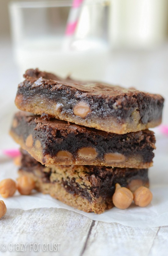 Stack of three Caramel Brownie Peanut Butter Cookie Bars on white wood table