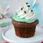chocolate cupcake with green frosting and whipped cream with straw sitting on mini cake plate