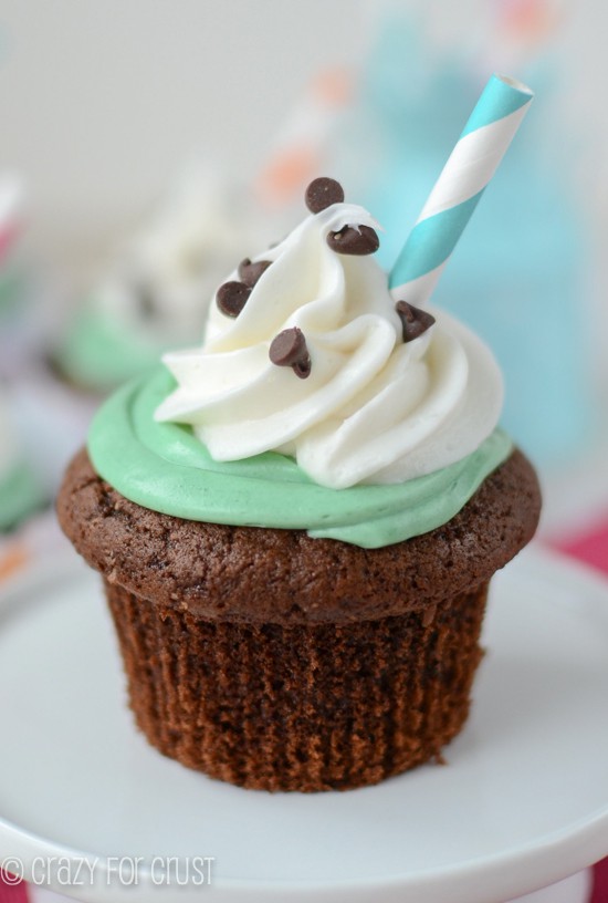 chocolate cupcake with mint frosting and whipped cream with straw sitting on mini cake plate