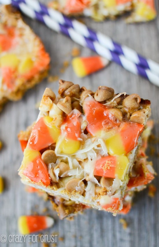 Overhead shot of Candy Corn Magic Bars on a wood table with candy corn and purple white striped straws